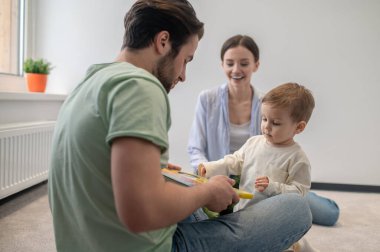 Birlikte oynuyoruz. Genç ebeveynler oğluyla oynuyorlar ve ona bir şey gösteriyorlar.