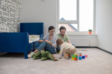 Oynuyorum. Ebeveynler pencerenin yanında oğullarıyla oynuyorlar.