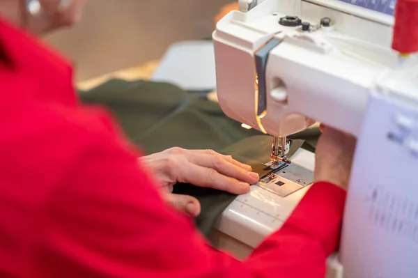 专业的 缝纫机上妇女坐在桌旁在织物上缝制整齐缝隙的后 侧视图 — 图库照片