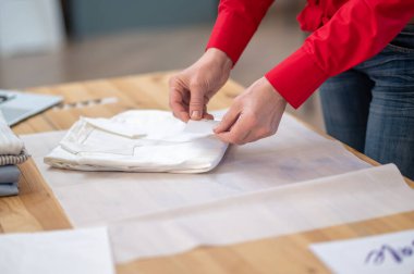 Yüksek kalite. Kadınların şefkatli elleri katlanmış beyaz elbiselere dokunuyor atölyedeki masa yüzeyinde ambalaj kağıdı üzerinde.