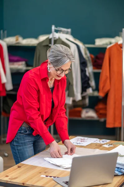 Werkstemming Grijsharige Glimlachende Vrouw Met Bril Buurt Van Tafel Vouwkleding — Stockfoto