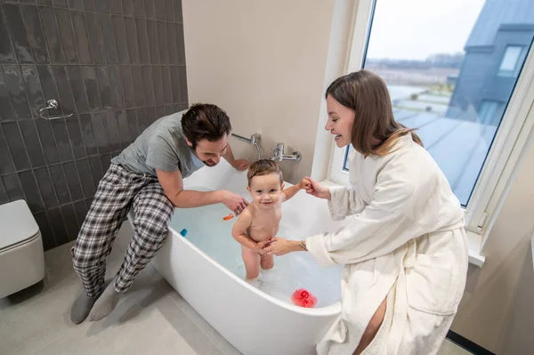 Tenderness Young Woman Sitting Bathtub Holding Hands Baby Smiling Camera — Stockfoto