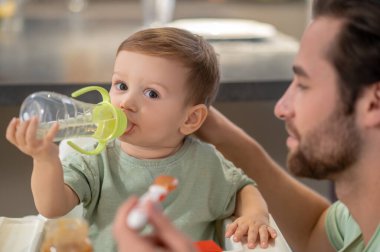 Yemek yiyorum. Şirin küçük çocuk, babası onu beslerken şişesinden su içiyor.