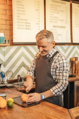 İlham. Önlüklü, beyaz saçlı mutlu bir adam kafesinin tezgahında duran tahtaları kesiyor.