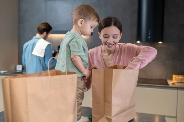 Food. Young mom with a little kid opening bags with food in the kitchen