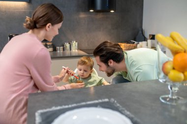 Bebeği besliyorum. Ebeveynler mutfakta tatlı bir çocuğu besliyor.