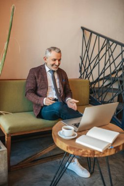 İlginç bir yer. Gri saçlı, orta yaşlı, kravatlı, neşeli bir şekilde laptop ekranına bakan, kahve masasında oturan, merdivenlerin yanında oturan çekici bir adam.