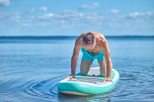 保持平衡 白发苍苍的高加索人跪在船桨板上 沐浴在晴朗的阳光下 — 图库照片