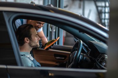 Araba teftişi. Araba denetimi için araba tamirhanesinde oturan genç bir tamirci.