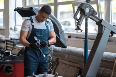 Odaklanmış Afro-Amerikan araba tamircisi kalibre lastik basınç göstergesini eldivenli elleriyle tutuyor.