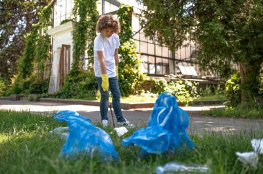 Eco volunteer. Curly-haired teen gathering garbage and looking involved