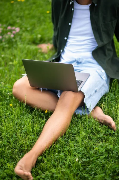Happy man. Barefoot man sitting on green grass outdoors with laptop spending free time without face