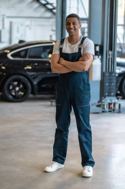 Full-size portrait of a smiling joyous auto mechanic in the work clothes standing at the service station