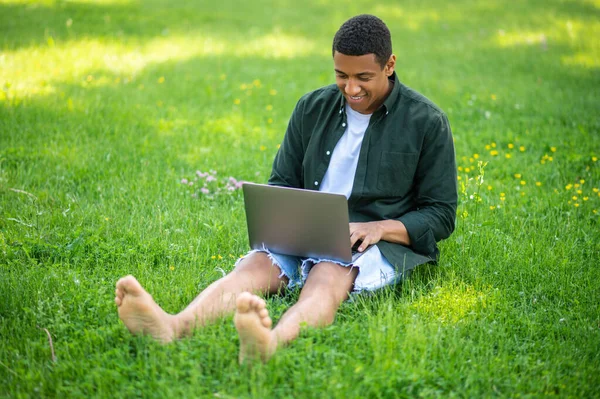 프리랜서 공원의 잔디에 노트북을 만들고 피부의 청년이 있습니다 — 스톡 사진