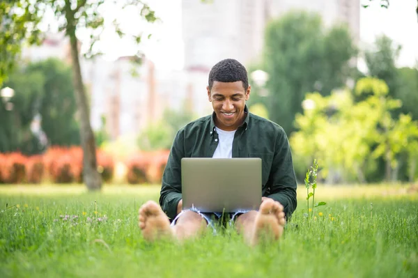 Feeling Great Dark Skinned Man Smiling Looking Laptop Sitting Grass — Stock Fotó