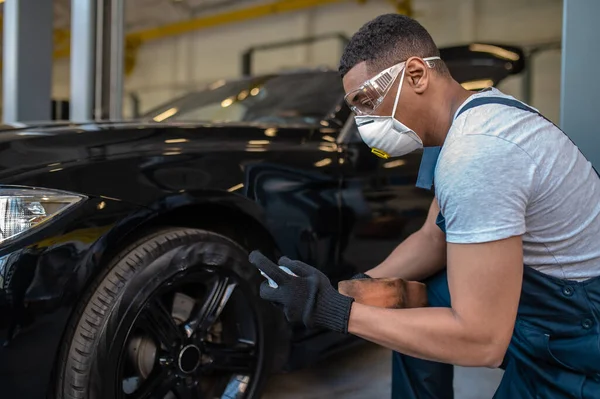 Qualified service station worker in the automotive respirator applying the black tire coating to the wheel surface