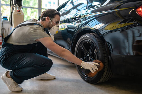 Skilled Caucasian service station worker polishing the rubber car wheel surface with a foam sponge