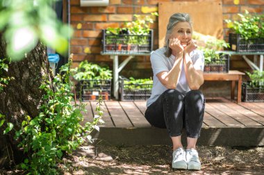 In thoughts. A woman in white tshirt sitting outside and looking thoughtful