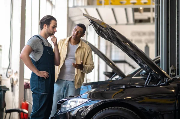 Question Thoughtful Caucasian Mechanic Touching Chin Looking Hood Dark Skinned — Foto Stock