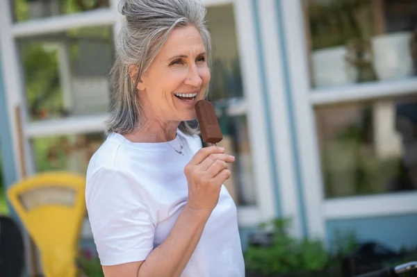 Eating ice-cream. A happy mature woman eating ice-cream and looking enjoyed