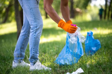 Temizlik, doğa. Güneşli bir günde yeşil parkta plastik çöp toplayan adamın elleri ve bacakları.