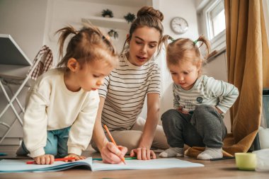 Female parent drawing with a colored pencil in the open sketchbook in the presence of her children