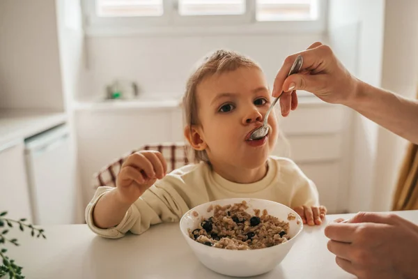 Caring Parent Giving Spoon Oatmeal Little Girl Seated Breakfast Kitchen — Stockfoto