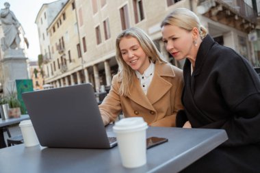 Gülümseyen genç bir kadın dizüstü bilgisayarında konsantre olmuş zarif bir bayana bir şey gösteriyor.