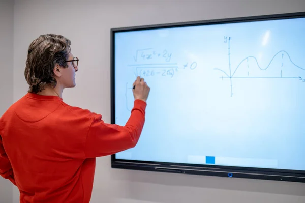 At the lesson. A teacher in red shirt writing on the board at the lesson