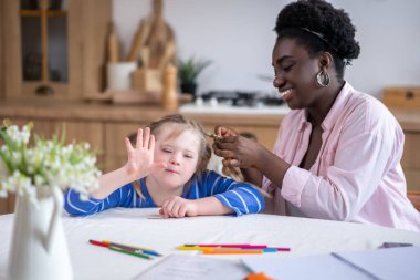 Doing hair. A smiling dark-skinned woman doing hair to the cute girl with down syndrome
