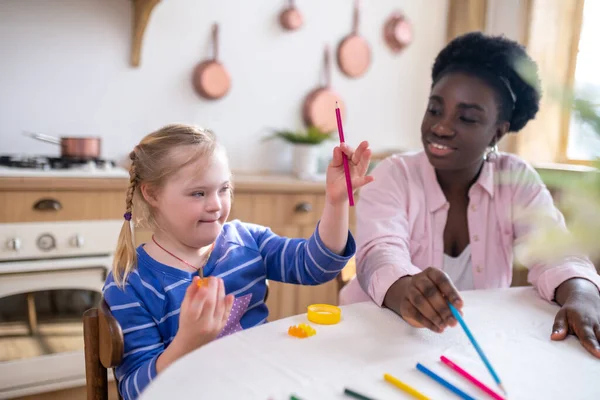 Home schooling. African american woman and a girl learning colors and drawing