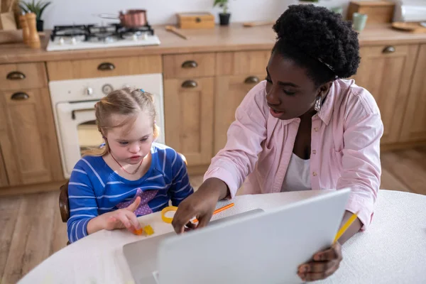 Home schooling. A girl with down syndrome having a lesson with her teacher and looking involved