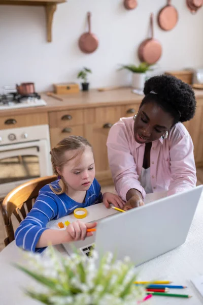 Home schooling. A girl with down syndrome having a lesson with her teacher and looking involved