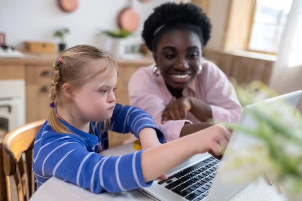 Home schooling. A girl with down syndrome having a lesson with her teacher and looking involved