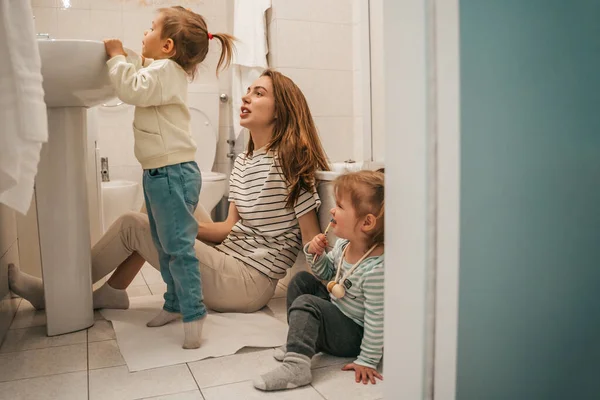 Young Mother Sitting Floor Bathroom While Her Daughters Brushing Teeth — Foto de Stock