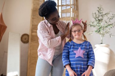 Little princess. African american woman putting a crown on head of a girl in blue dress