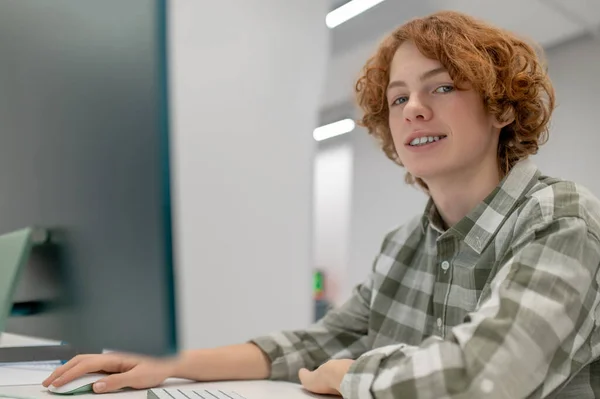 IT lesson. A ginger schoolboy sitting at the computer at school and looking involved