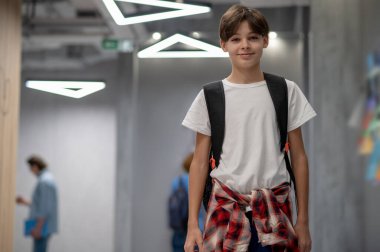 At school. A boy in white tshirt with ackpack in a school corridor