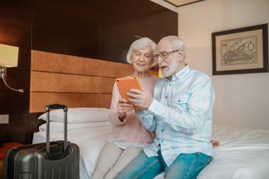 On internet. Senior couple sitting on a bed and watching something on a talet
