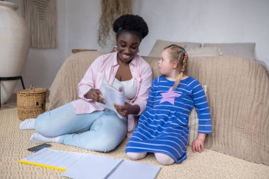 Dark-skinned woman reading something to a girl with down syndrome