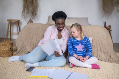 Dark-skinned woman reading something to a girl with down syndrome