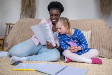 Dark-skinned woman reading something to a girl with down syndrome