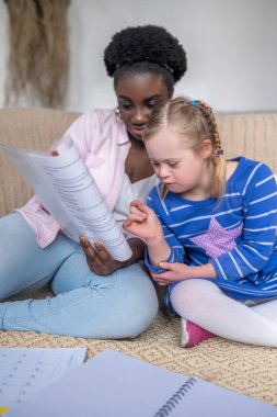 Dark-skinned woman reading something to a girl with down syndrome