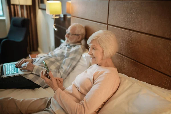 Online. Senior couple lying in bed watching something online