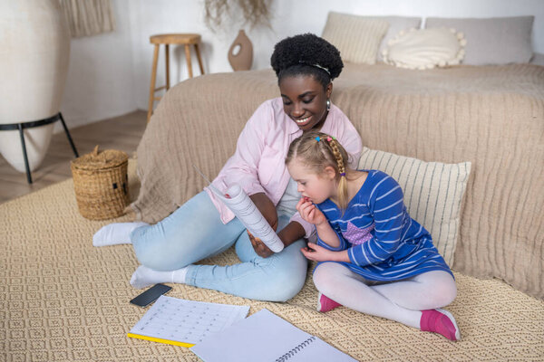 Dark-skinned woman reading something to a girl with down syndrome