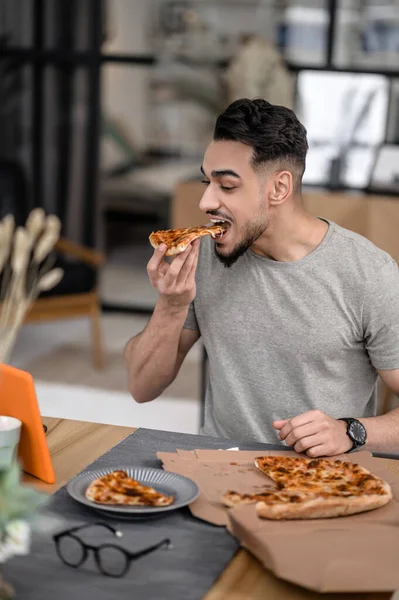 Eating Home Happy Young Bearded Man Biting Pizza Looking Interestedly — Foto de Stock