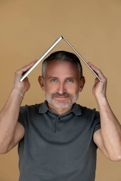 Mental health. Mid aged man holding his laptop as a roof