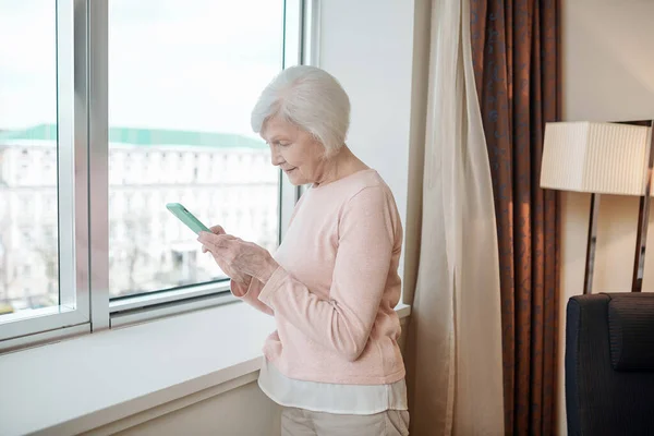 Online Pleasant Looking Senior Lady Texting Looking Involved — Stockfoto