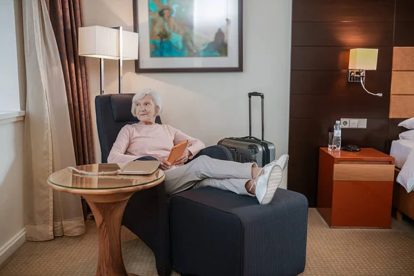 Thinking. Gray-haired woman holding a tablet and looking thoughtful