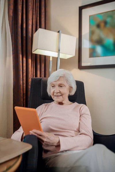Modern technologies. Elderly lady in beige blouse with a tablet in hand